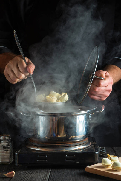 Chef professionnel prépare pelmeni dans une casserole dans la cuisine. Gros plan des mains d'un cuisinier pendant qu'il travaille - Photo, image