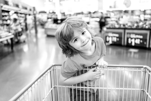 Funny customer boy child holdind trolley, shopping at supermarket, grocery store. - Фото, зображення