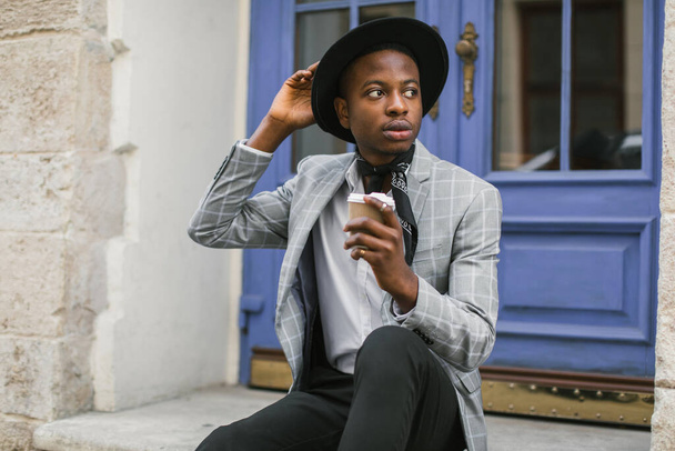 African guy in suit sitting outdoors with cup of coffee - Photo, image