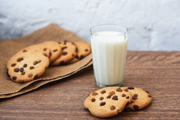Fragrant, tasty, homemade cookies in nonwoven brown fabric with raisins and a glass of fresh milk on the table. Delicious, hearty, healthy breakfast. Copy space, high resolution - Foto, afbeelding
