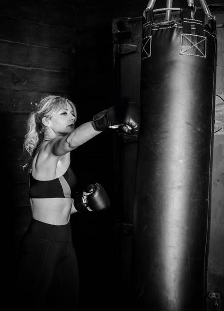 Woman hits the heavy bag with a strong kick. Concept about fit box, martial arts and sport. She is fighter for success. - Foto, Imagen