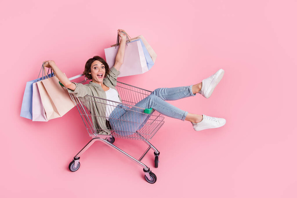 Full body photo of carefree funky person sit in trolley hold packages isolated on pink color background - Fotó, kép
