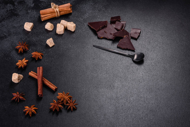 Broken black chocolate pieces with star anise and cinnamon on black background - Photo, Image