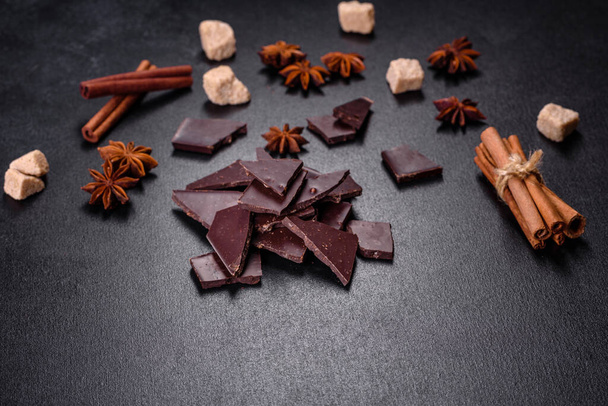 Zerbrochene schwarze Schokoladenstücke mit Sternanis und Zimt auf schwarzem Hintergrund - Foto, Bild