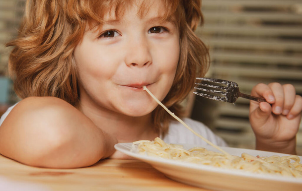 Caucasian smiling child eating pasta, spaghetti, portrait close up. Kids face. - 写真・画像