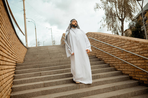 An arabian man in white traditional clothing on the stairs - Фото, изображение