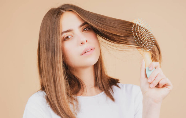 Young beautiful woman combing hair. Hair Care. Beautiful brunette woman hairbrushing hair with hairbrush. Brushing healthy hair with comb. - 写真・画像