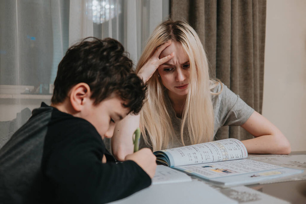 Kızgın anne ve oğlu ödev yapıyor. Kız kardeş, erkek kardeşin matematiği çözmesine yardım eder. Evde eğitim. - Fotoğraf, Görsel