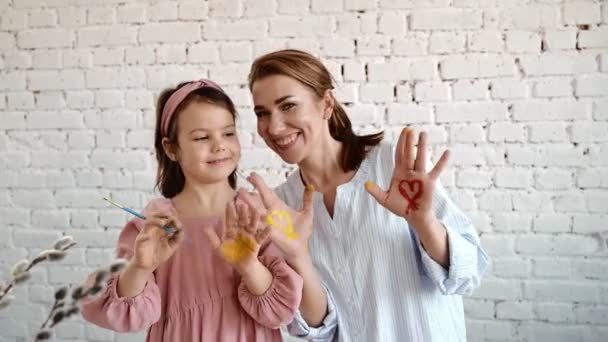 Young mother and brunette daughter overjoyed smiling and painting palms with paint. - Footage, Video