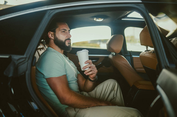 A young with a coffee cup sitting in a car - Photo, Image