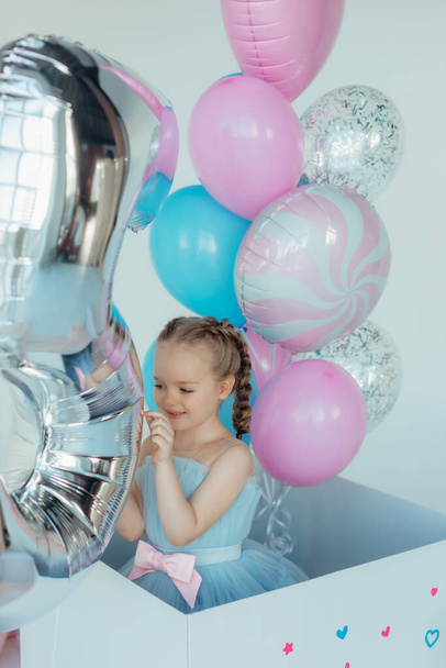 Mavi elbiseli sevimli, gülümseyen küçük kız. İyi ki doğdun Doğum günü prensesi bir balon zeminine karşı pastayla. Hediyelik eşya dükkanı. Alışveriş günü. Çocukluk ve komik kutlama konsepti. - Fotoğraf, Görsel