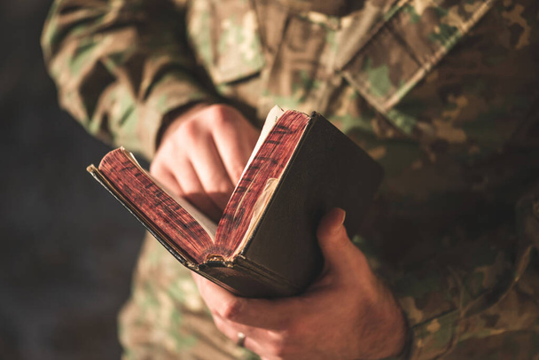 Soldado vestido com uniforme de camuflagem segurando uma bíblia em sua mão. Soldado lendo e meditando a Palavra de Deus - Foto, Imagem