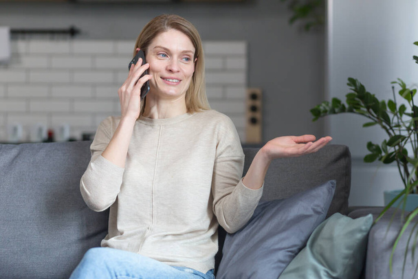 Happy woman at home, sitting on the couch and talking on the phone - Фото, зображення