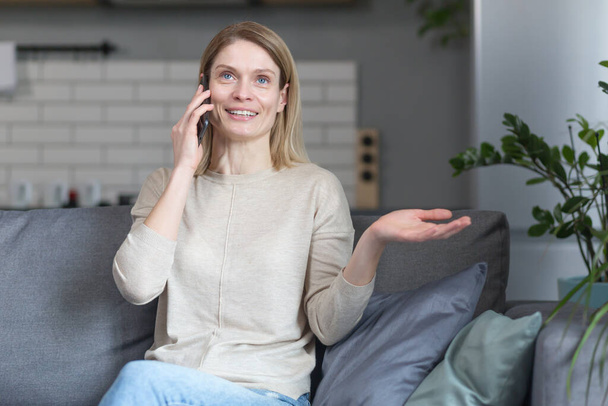 Happy woman at home, sitting on the couch and talking on the phone - Foto, Bild