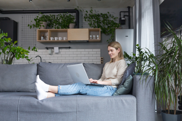Woman sitting at home on the couch in the kitchen, using a laptop for a video call, talking to friends remotely - Foto, Bild