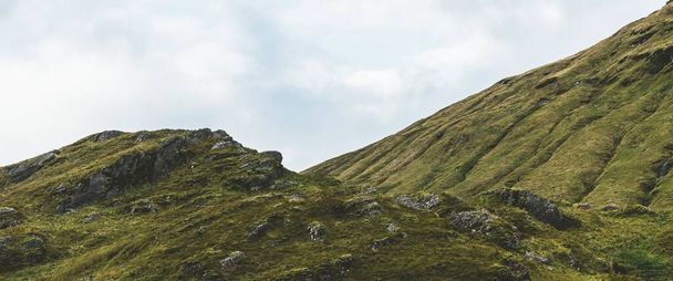 劇的な青い空の下で緑の岩の海岸と丘。ロッホ・ロンゴンドとトラサックス国立公園、インナー・ヘブリディーズ、スコットランド、英国。旅行先,エコツーリズム,ハイキング,レジャー活動 - 写真・画像