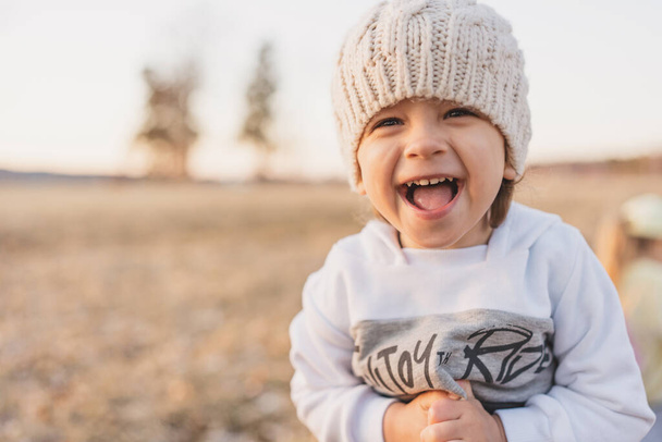 little boy smile and scream in knitted hat in sunlight, portrait of happy child outdoors walk in field - Photo, Image