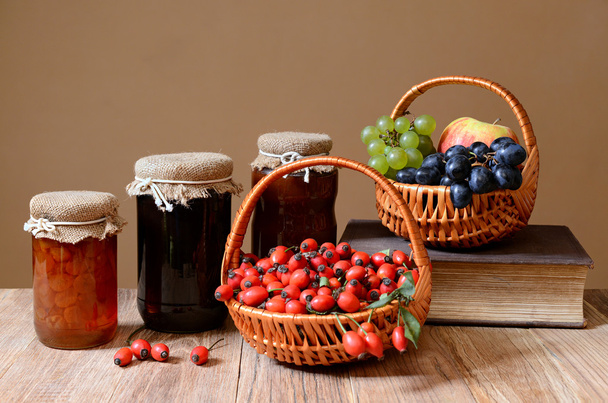 Rosehips in wicker baskets, fruit and jam in a jar - Foto, afbeelding