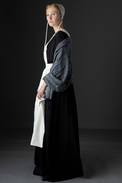 An Amish woman wearing a black dress with a white apron, cap, and shawl - Фото, изображение