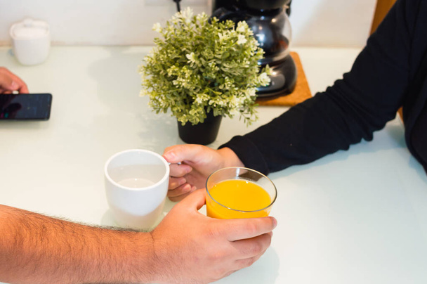 husband and wife holding cups with juice next to each other on the counter, caucasian couple in the kitchen at home in a loving moment together at breakfast. - Foto, imagen