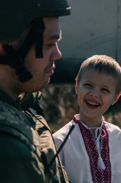 ウクライナの兵士の近くの刺繍シャツの子供の少年の肖像画。ウクライナにおけるロシアの軍事侵攻の概念。ウクライナとヨーロッパでの戦争。子供と戦争. - 写真・画像