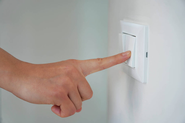 Desperdício de Energia. dedo feminino é desligar no interruptor de iluminação. - Foto, Imagem
