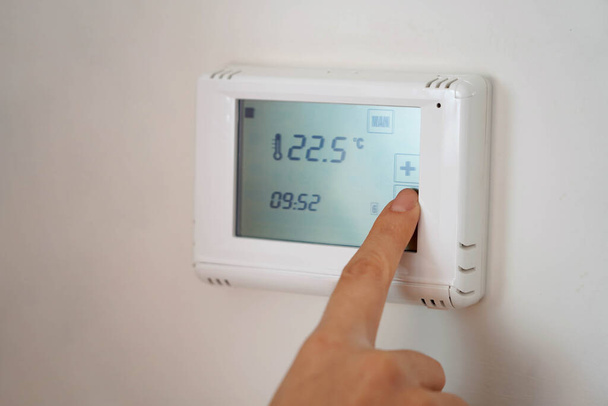 Conceito de poupança de energia: mão humana a baixar a temperatura no visor digital - Foto, Imagem