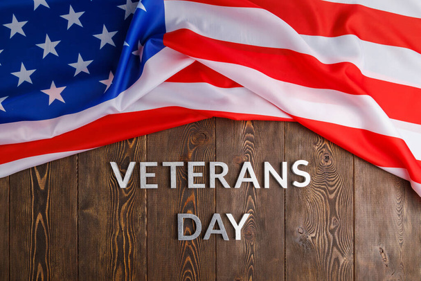 the words veterans day laid with silver metal letters on wooden board surface with crumpled usa flag - Fotó, kép