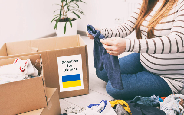 the pregnant woman is sorting baby clothes with desire to donate its for Ukrainian refugees - Фото, зображення