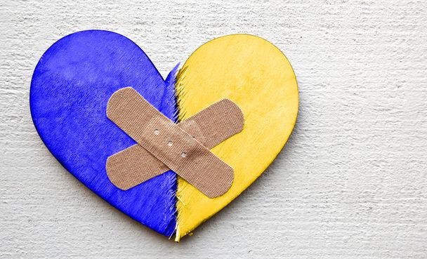 Two parts of broken wooden heart in colors of Ukrainian flag taped by a patch.  - Valokuva, kuva