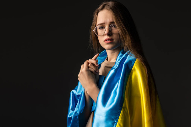 Woman holds ukrainian blue and yellow flag on black background. - Foto, imagen