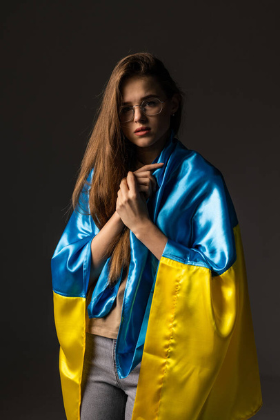 Sad woman covered with Ukraine flag. Concept of standing with Ukrainian nation in war with Russia. - Photo, Image