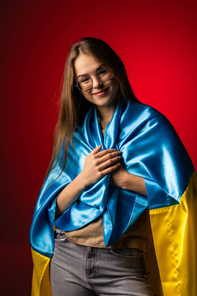 Молода жінка, вкрита національним прапором України на червоному фоні. - Фото, зображення