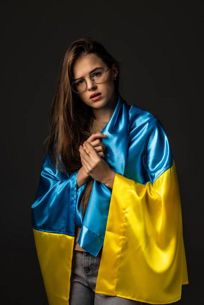 Sad woman covered with Ukraine flag. Concept of standing with Ukrainian nation in war with Russia. - Foto, afbeelding