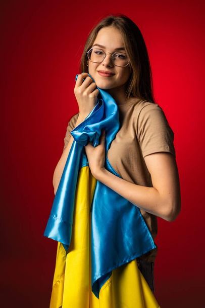 Jovem mulher coberta com a bandeira nacional da Ucrânia sobre fundo vermelho - Foto, Imagem