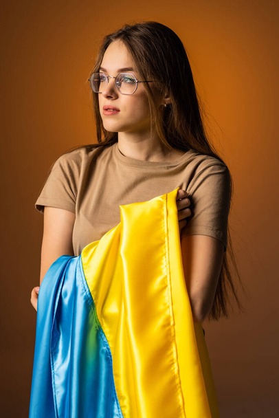 Young woman with Ukraine national flag standing over orange background. - 写真・画像