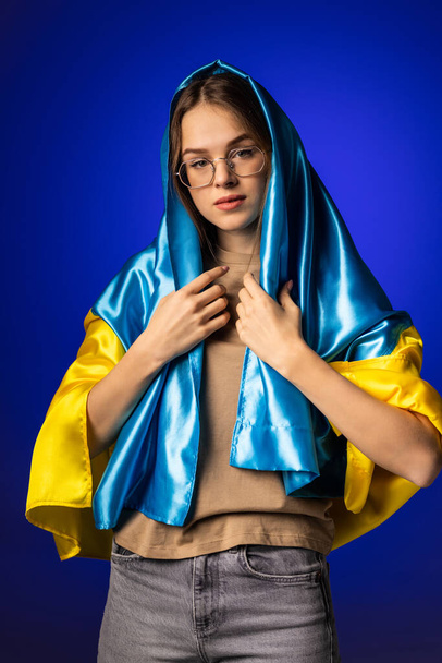 fiatal nő Ukrajna nemzeti zászló felett áll a kék háttér. - Fotó, kép
