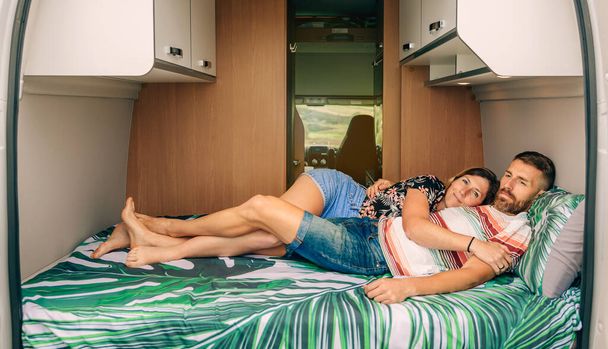 Para odpoczywająca w łóżku swojego kampera z splecionymi nogami - Zdjęcie, obraz