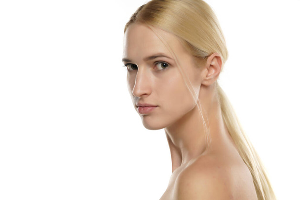 Vue latérale d'une jeune femme blonde sans maquillage, et avec les cheveux attachés sur un fond blanc - Photo, image