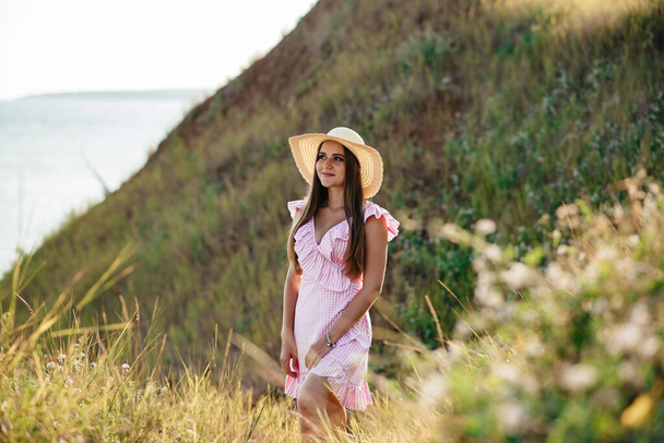 the girl runs across the field. Happy girl. Long hair. White dress. A hat with a brim. Bouquet of daisies. A young girl in nature. - Foto, Bild