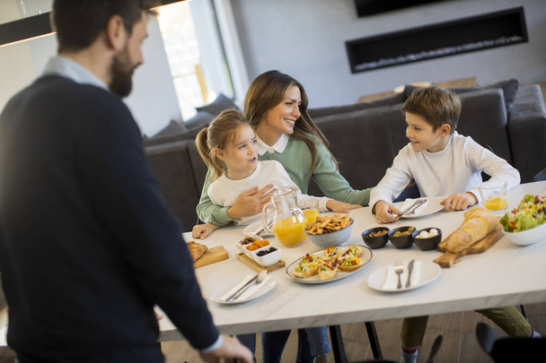 Νεαρή ευτυχισμένη οικογένεια μιλάμε, ενώ έχοντας πρωινό στο τραπέζι στο διαμέρισμα - Φωτογραφία, εικόνα