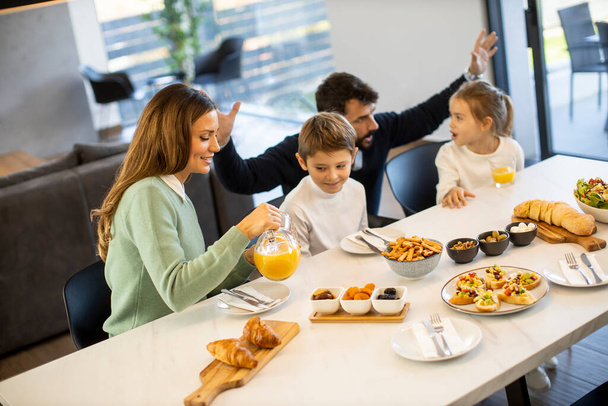 Giovane famiglia felice parlando mentre fa colazione al tavolo da pranzo in appartamento - Foto, immagini