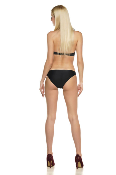 Rear view of a young blond woman posing in swimsuit on a white background - Foto, Imagem