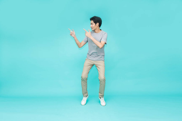 Young Asian man jumping and pointing to empty copy space isolated on green background - Valokuva, kuva