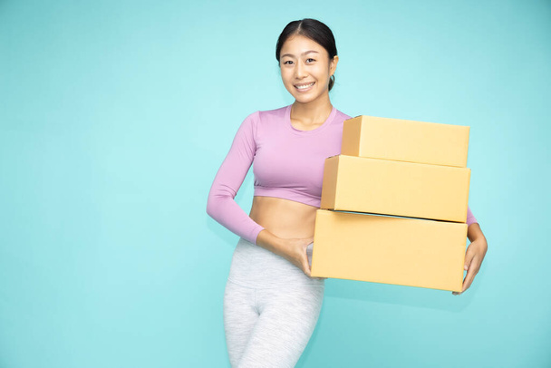 Happy Asian sporty woman  holding package parcel box isolated on green background, Delivery and shopping express concept - Фото, зображення