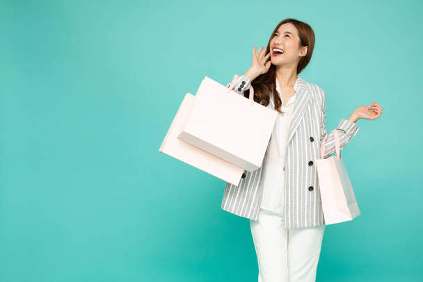 緑の背景に隔離された薄緑のショッピングバッグを保持スーツの幸せな若いアジアのビジネス女性 - 写真・画像