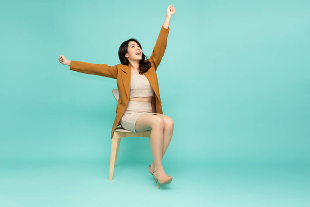 Ελκυστική όμορφη Ασιάτισσα επιχειρηματίας κάθεται σε λευκό μοντέρνα καρέκλα και τα χέρια ψηλά τα χέρια από την ευτυχία, Ενθουσιασμένος επιχειρηματίας νικητής έννοια επιτυχίας - Φωτογραφία, εικόνα