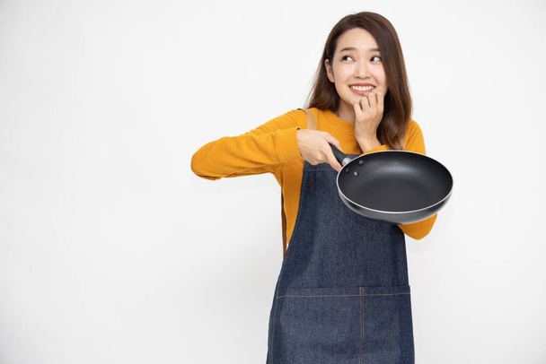 Glückliche junge asiatische Hausfrau trägt Küchenschürze Kochen und hält Pfanne isoliert auf weißem Hintergrund - Foto, Bild