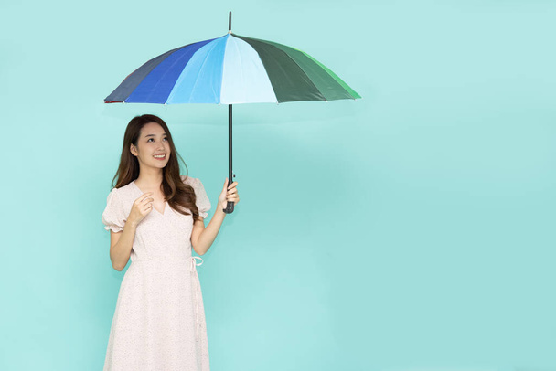 Молодая азиатка держит зонтик, стоящий изолированно на зеленом фоне - Фото, изображение