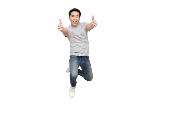 Νεαρός Ασιάτης πηδάει και δείχνει τους αντίχειρες του απομονωμένους σε λευκό φόντο - Φωτογραφία, εικόνα